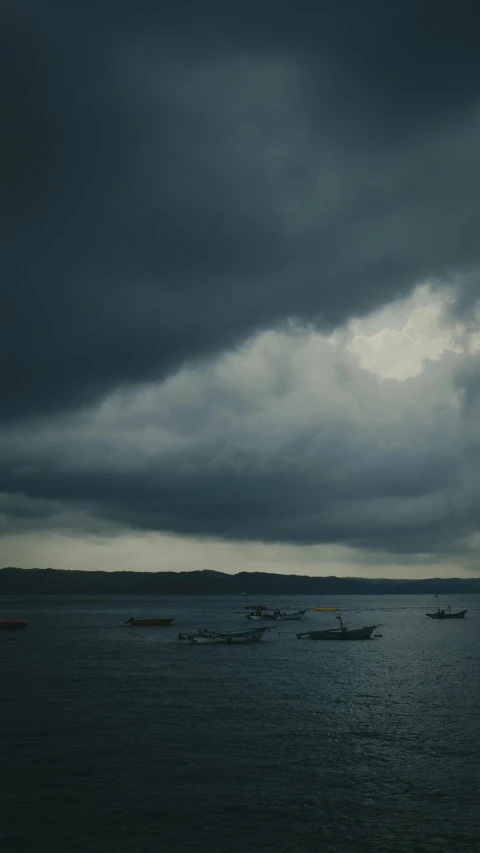 some small boats out on the ocean under some stormy skies