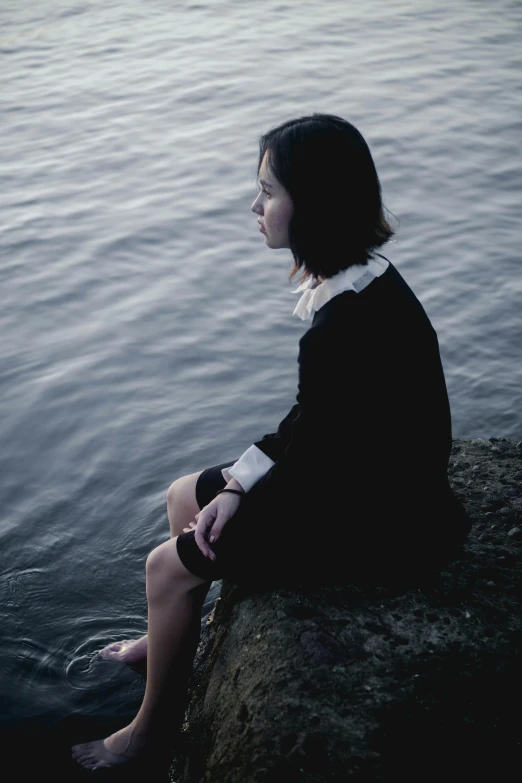 a woman sitting on a cliff next to the water