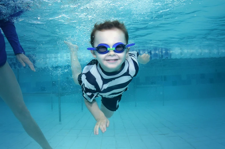 a young child in sunglasses swimming under a pool