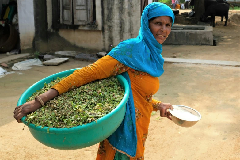 woman holding a large blue bucket of grass