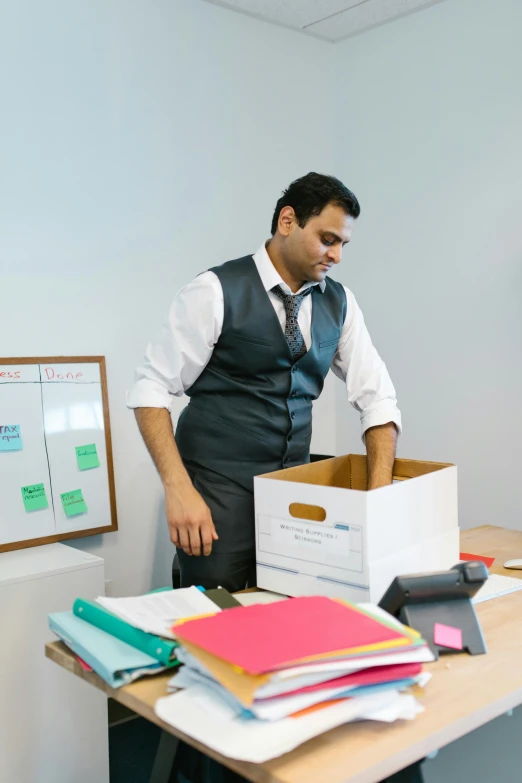 a man in a tie and a black vest is standing next to a table with lots of files