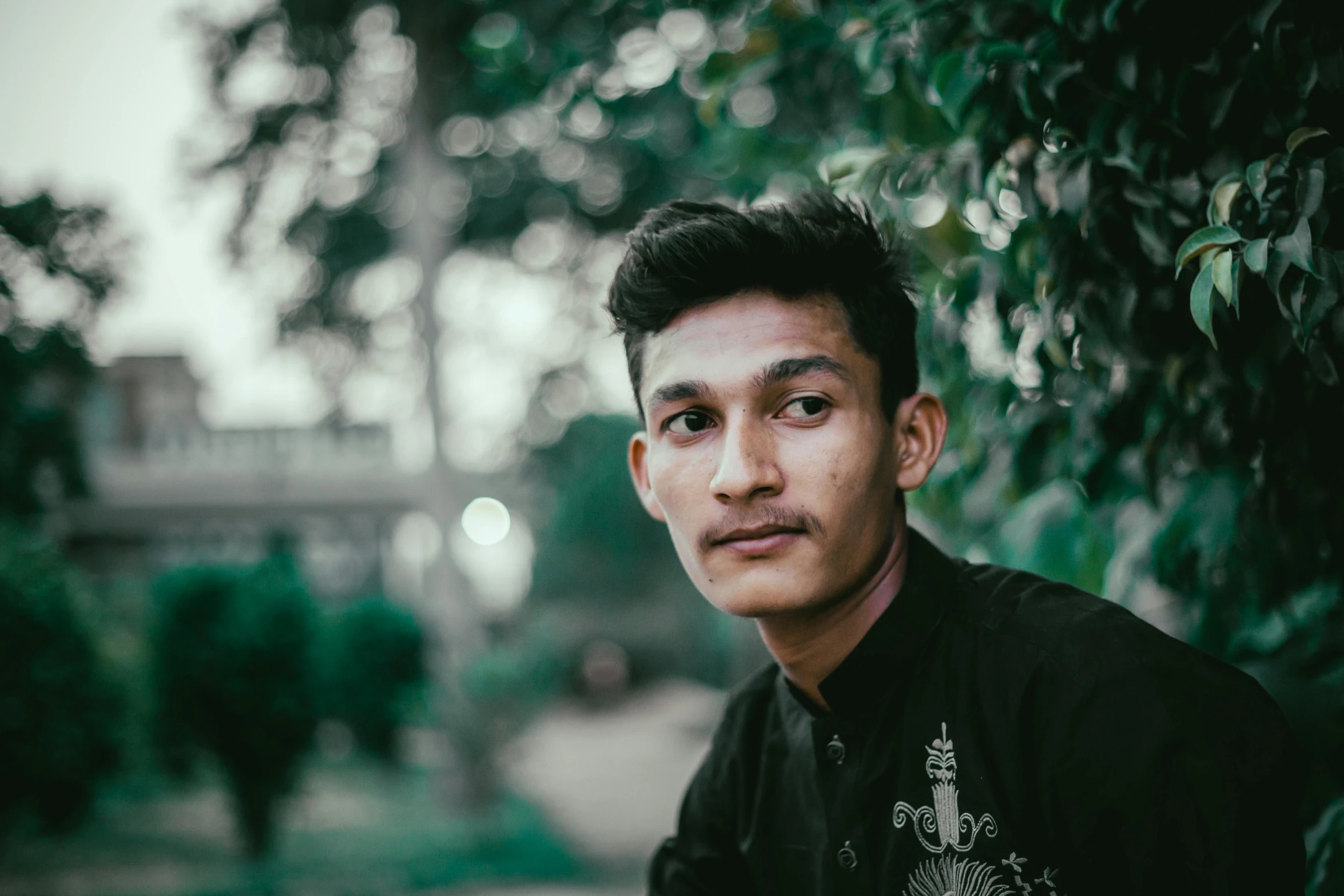 a young man sitting near some leaves with his eyes closed