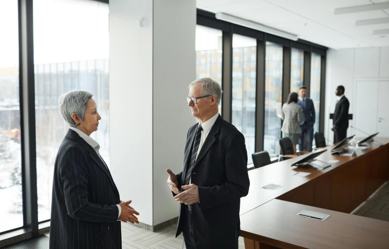 two men talk in an office with a glass wall behind them