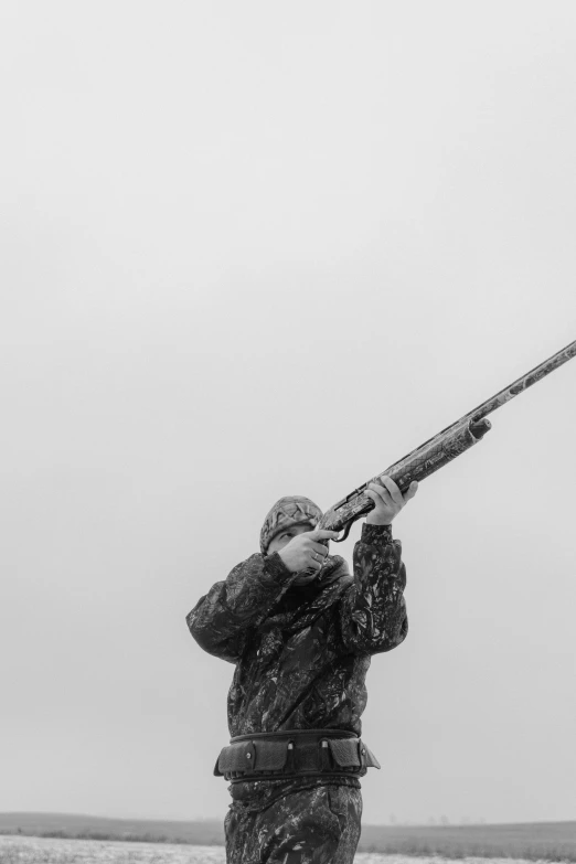 a man standing on top of a snow covered field holding onto a gun