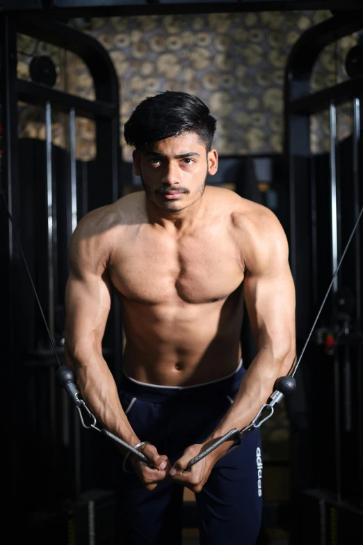 a shirtless man is holding on to ropes in the gym