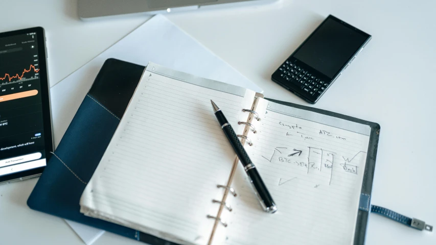 a notebook, pen, and cell phone on a table