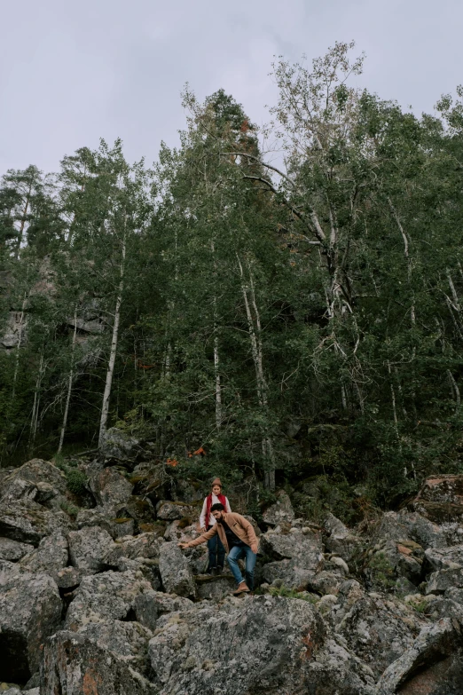 a man and woman sitting on rocks in the woods