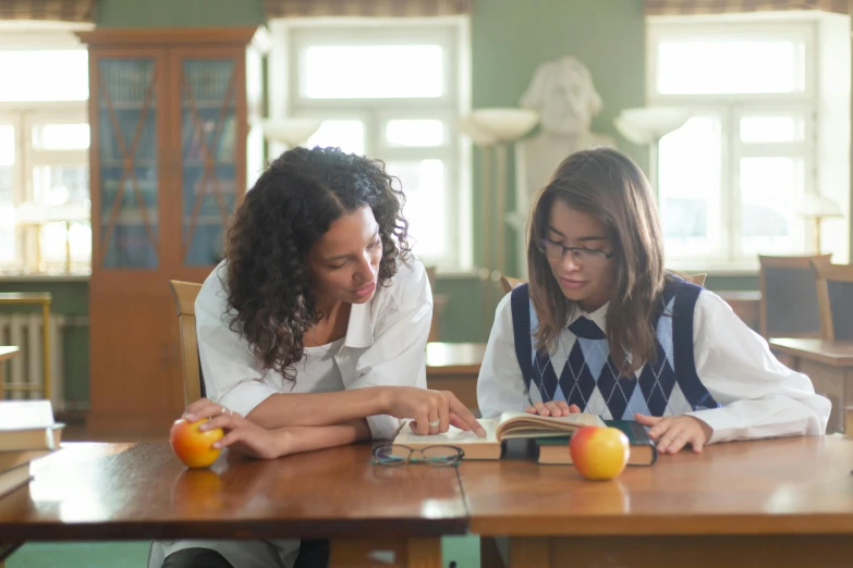 two girls reading books at a table with oranges on it