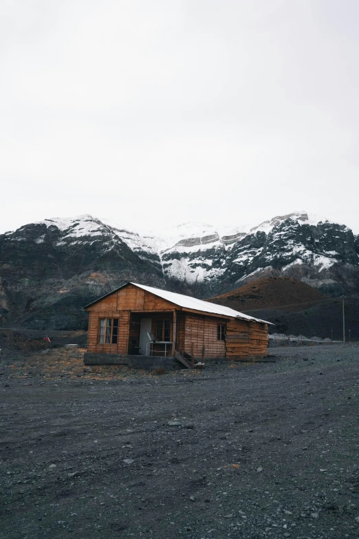 a small wooden building with a snowy mountain behind it