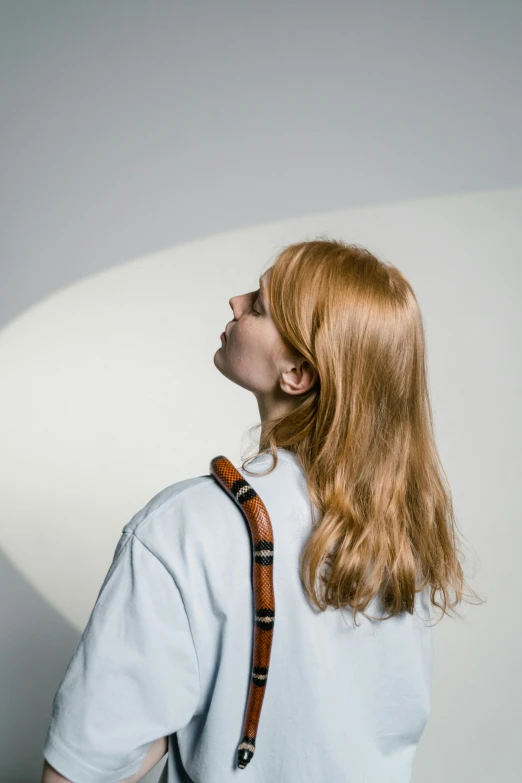 a young woman with long red hair and white shirt is standing near a white wall