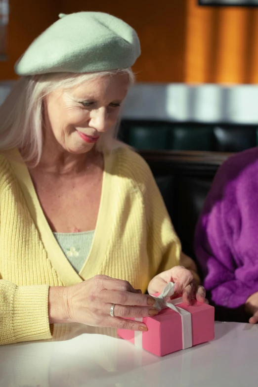 two women are sitting around looking at a pink present box