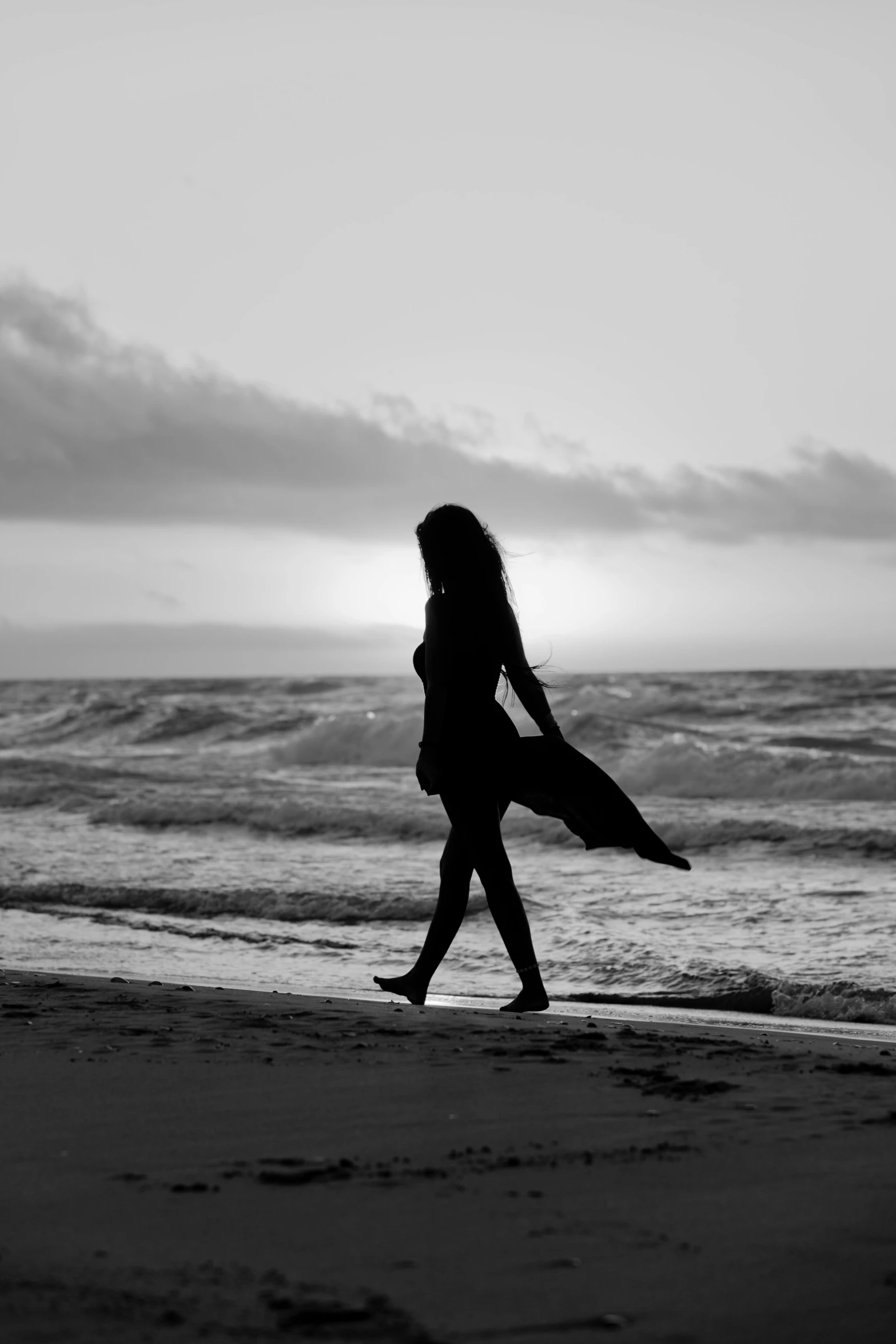 a woman walks on the beach in silhouette with her back turned to the camera
