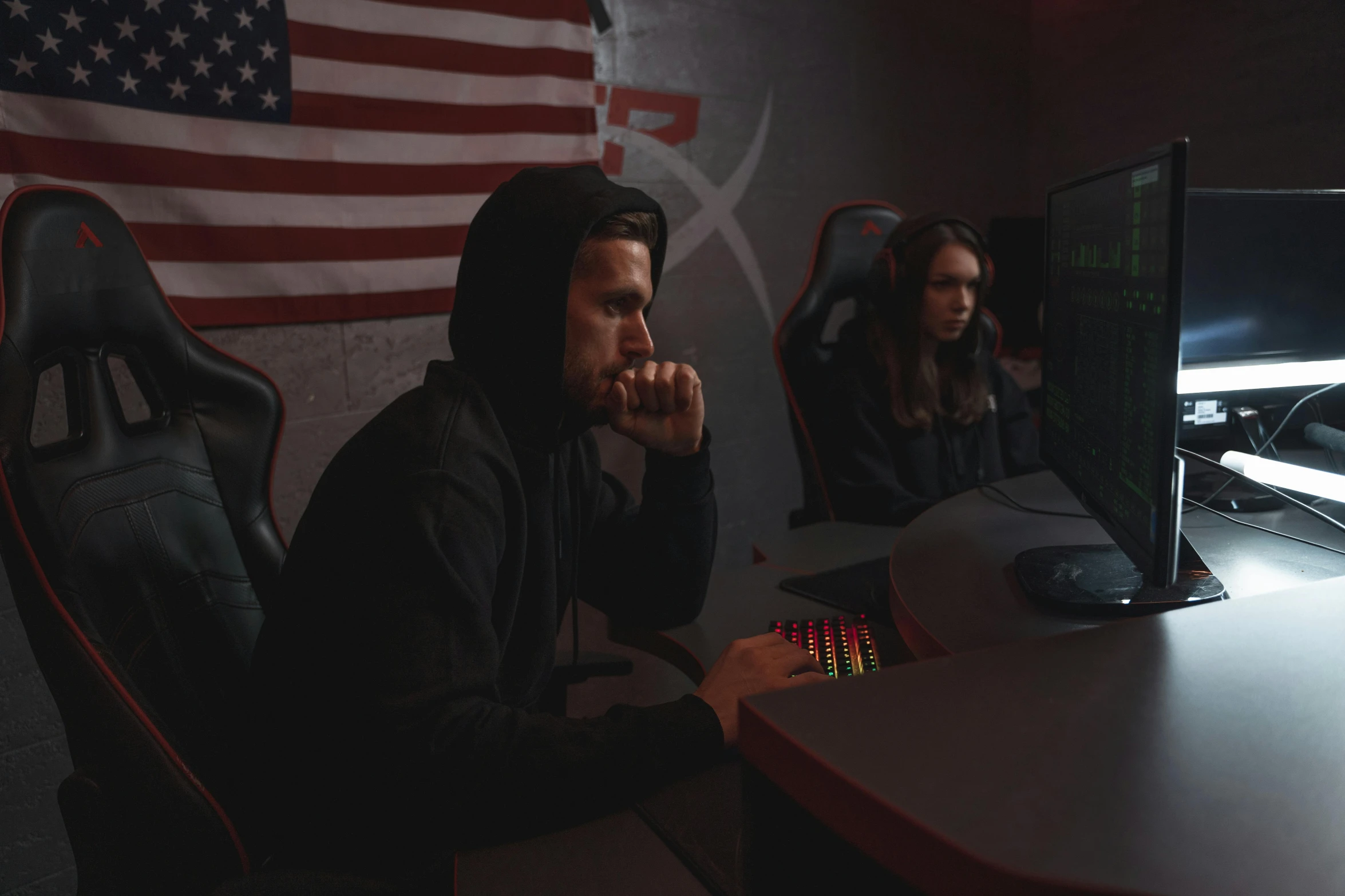 two people sitting at a computer table in front of a us flag