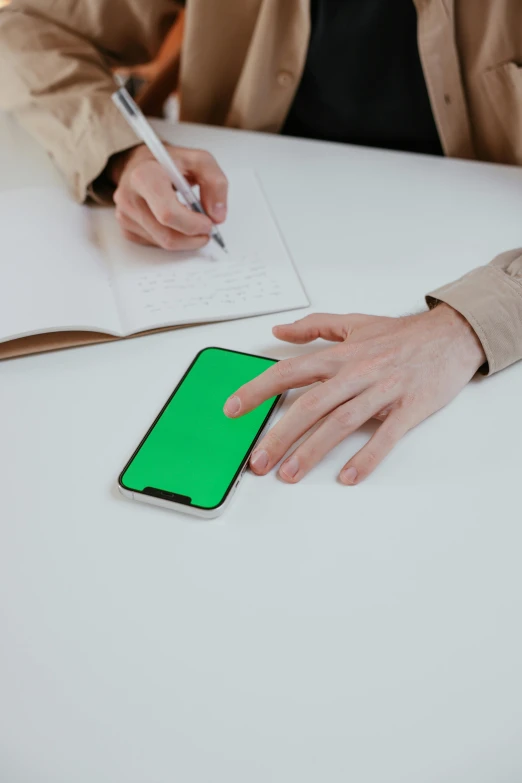 two hands using a green cell phone on a table