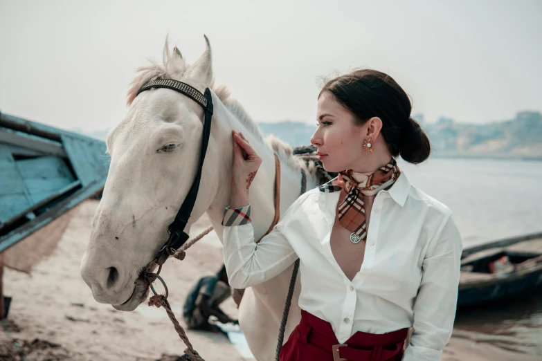 a lady holding onto her white horse by the river