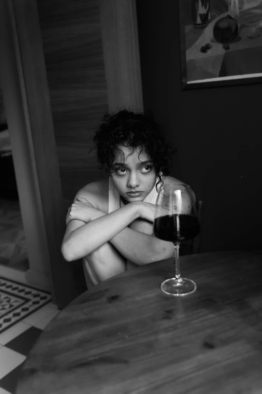 a young woman sitting at a table with her arms crossed next to a wine glass