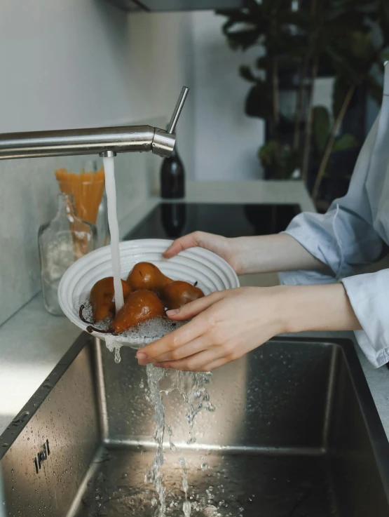 a person holding a bowl of apples over a sink