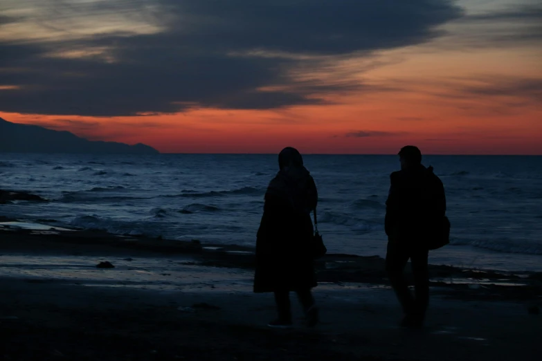 two people standing on the beach at sunset looking out to sea