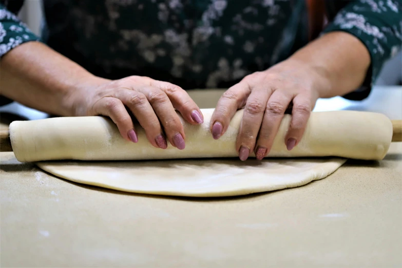 a woman kneads dough onto a rolling pin on top of a table