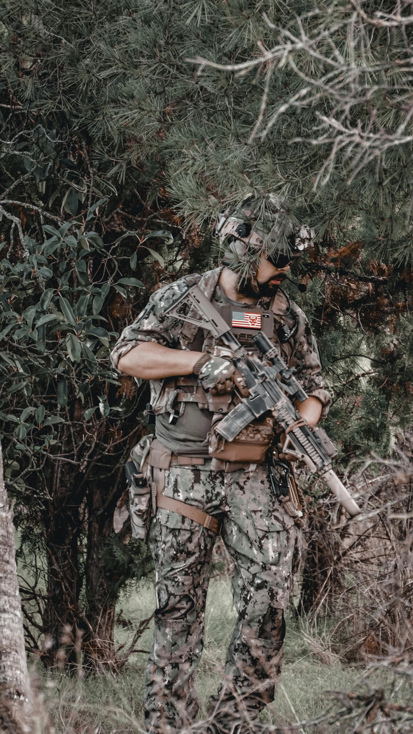 soldier with gun, camouflaged in green bushes looking in trees