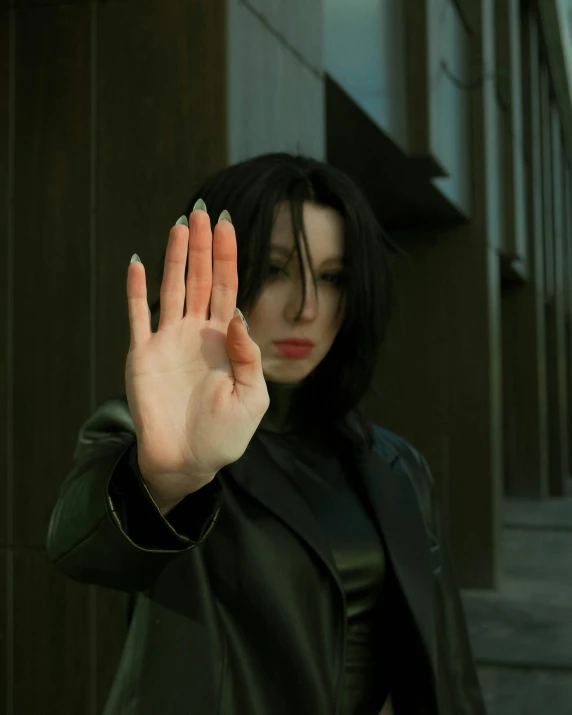 a woman with black hair and wearing a black coat holds her hand up in the air