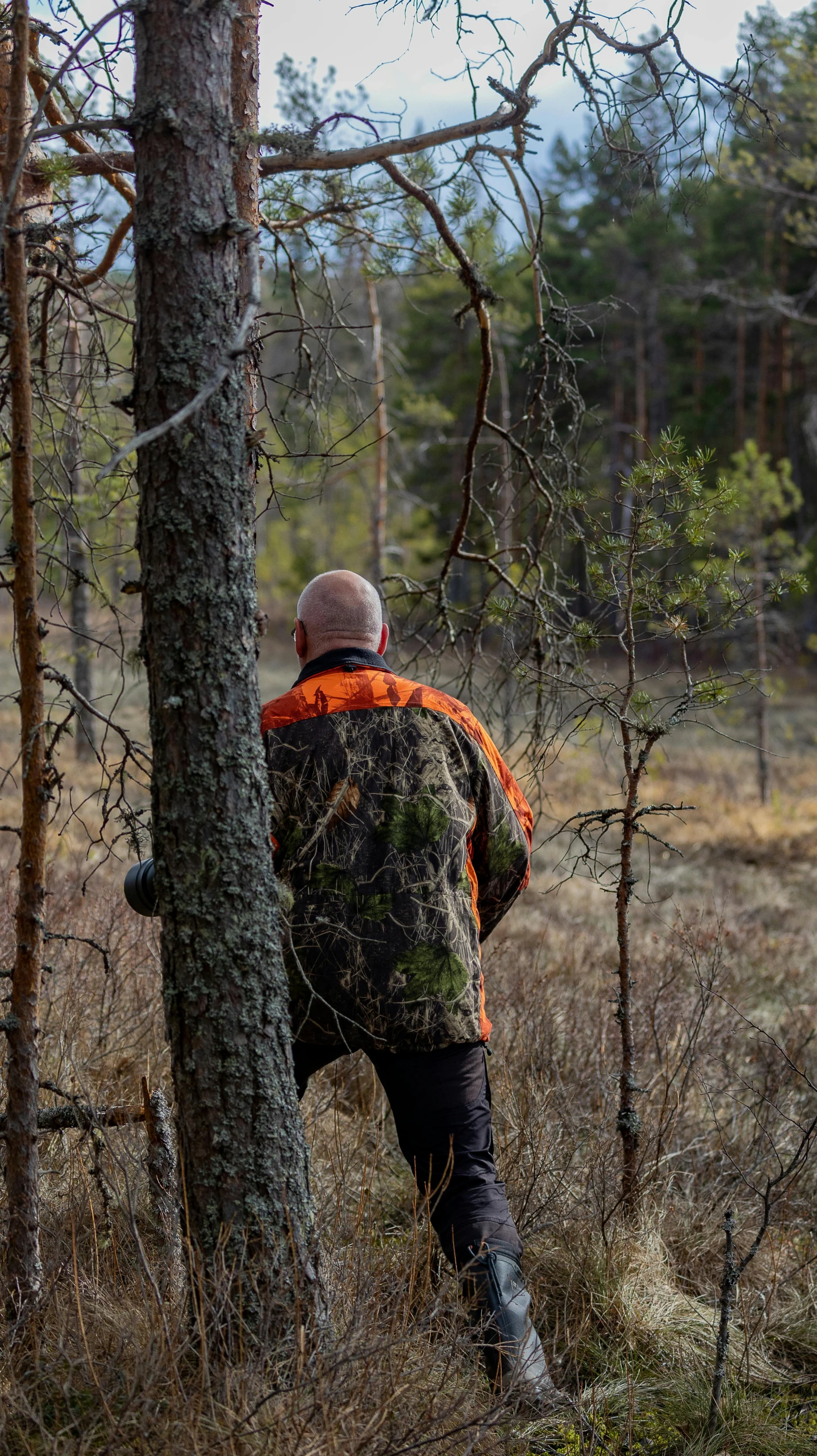 man in camouflage jacket looking at trees through nches