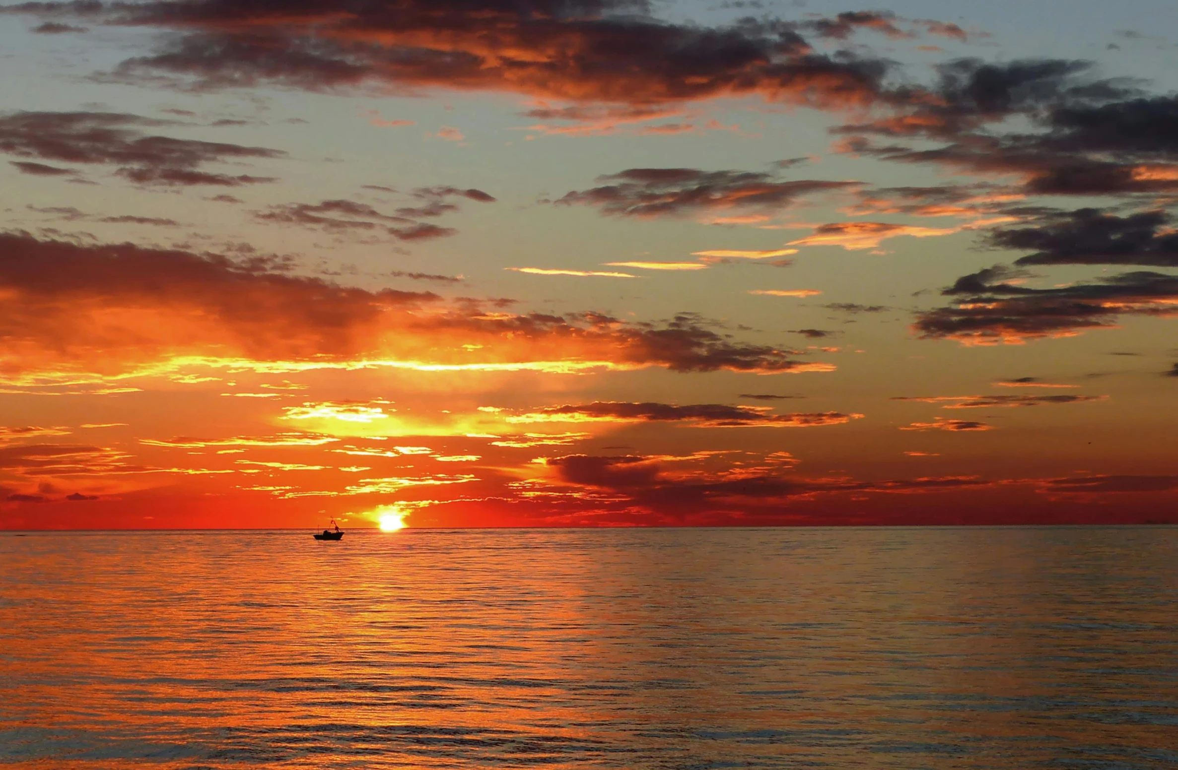 a small boat at sea while the sun sets