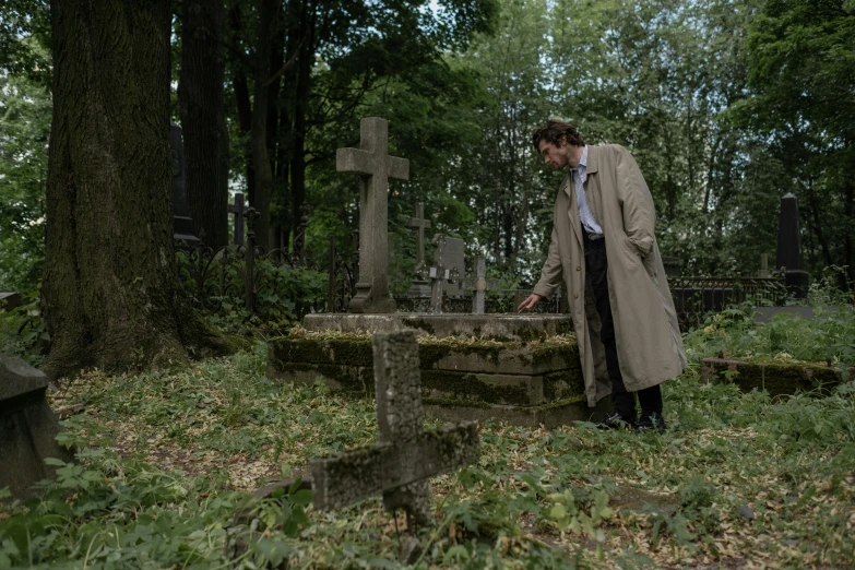 a man in a trench coat leaning over a grave