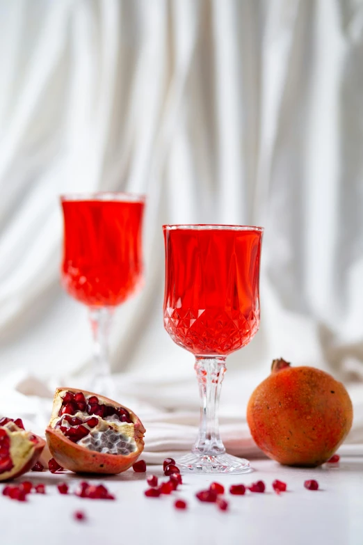 two glasses of wine with one half cut open with some pomegranate on top of the glass