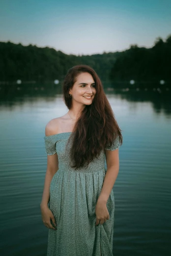 a beautiful woman standing by a lake wearing a dress