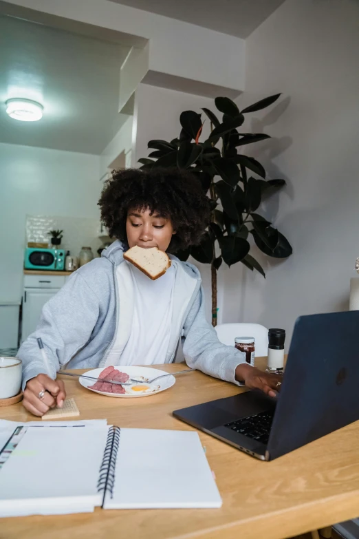 a woman is seated at a desk while eating a sandwich