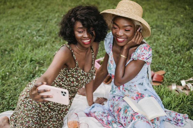 two young woman in colorful dress sit on blanket and hold phones