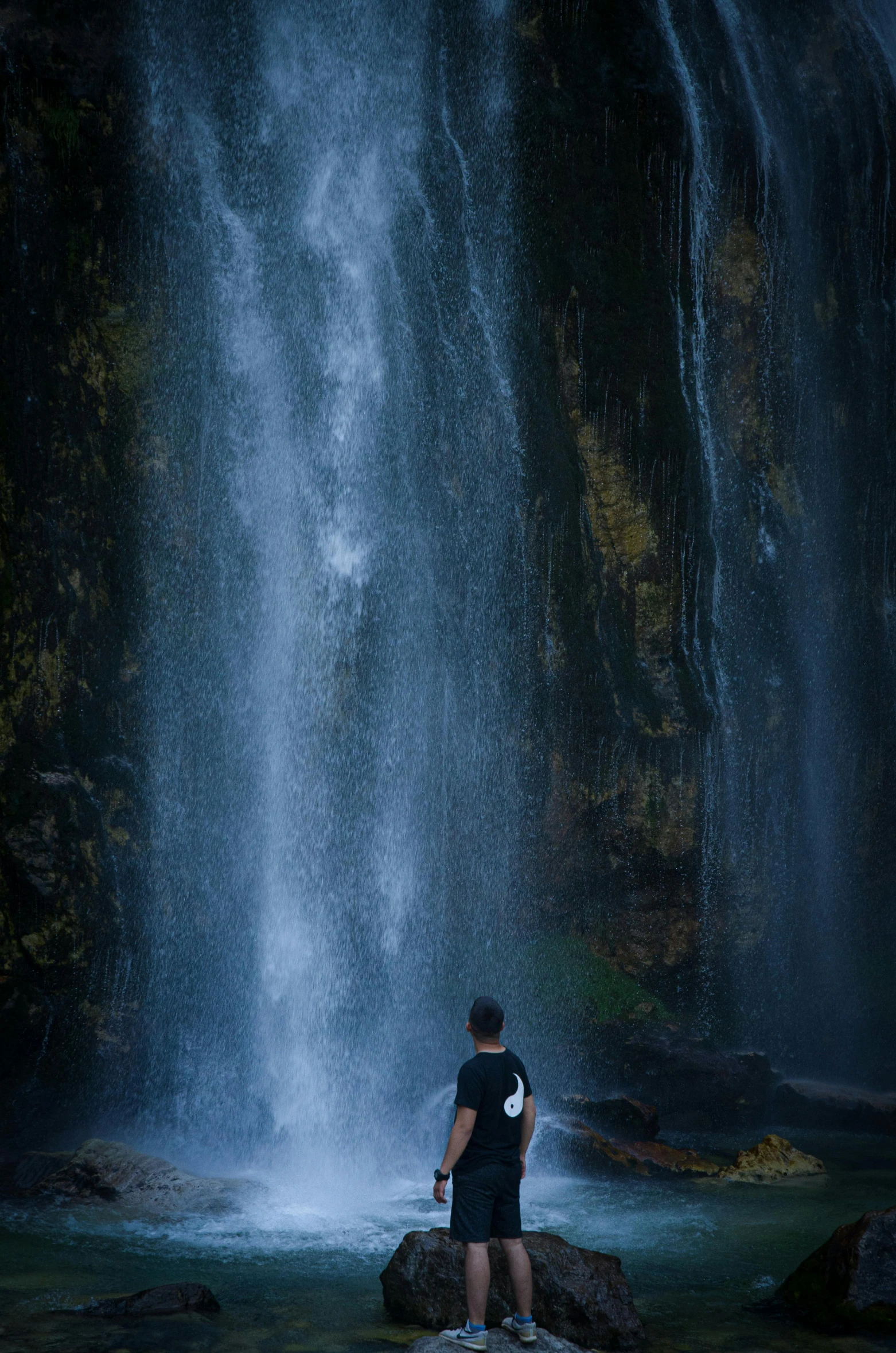 a man standing in front of a tall waterfall