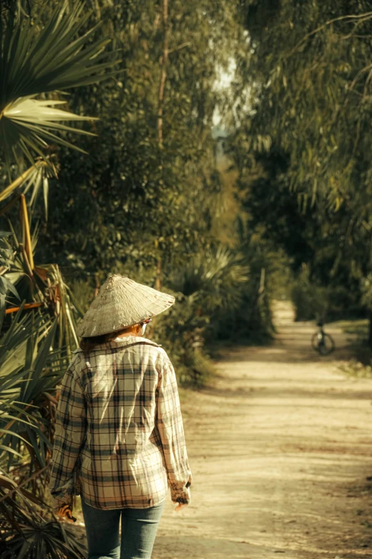 a woman in a straw hat walks down a dirt road