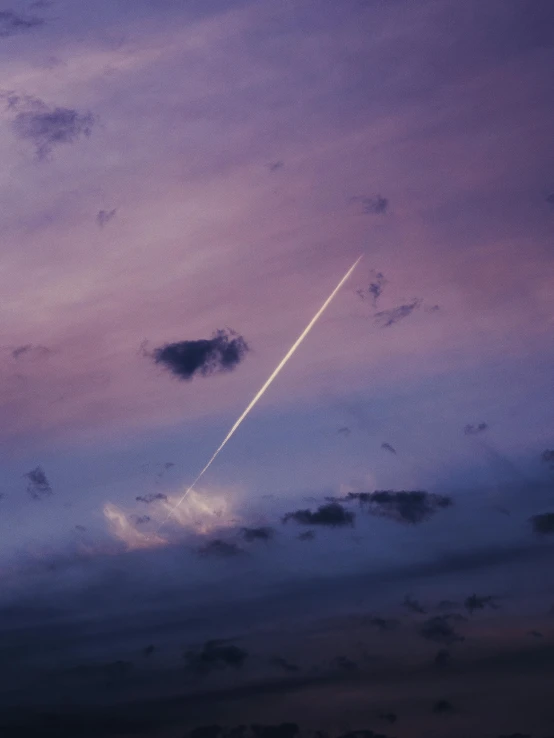 an airplane flying up in the sky at dusk