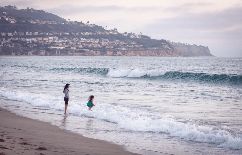 a woman and child playing in the waves at the beach