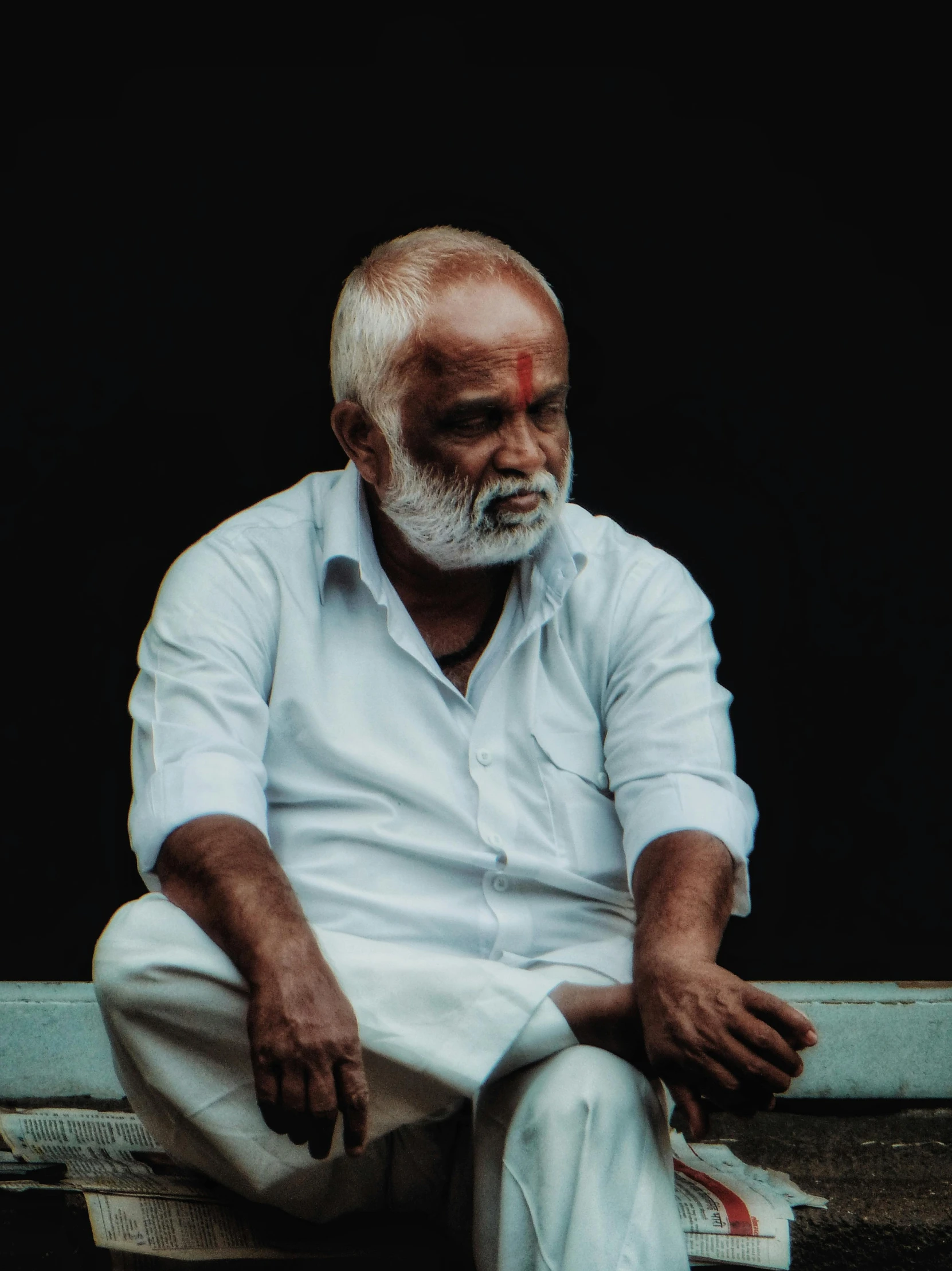 an older man with white hair wearing white shoes sits in a doorway