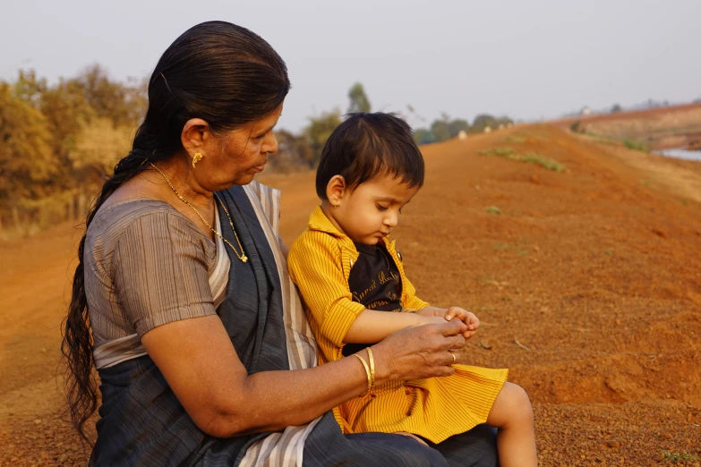 a woman and her little boy sitting on a dirt road