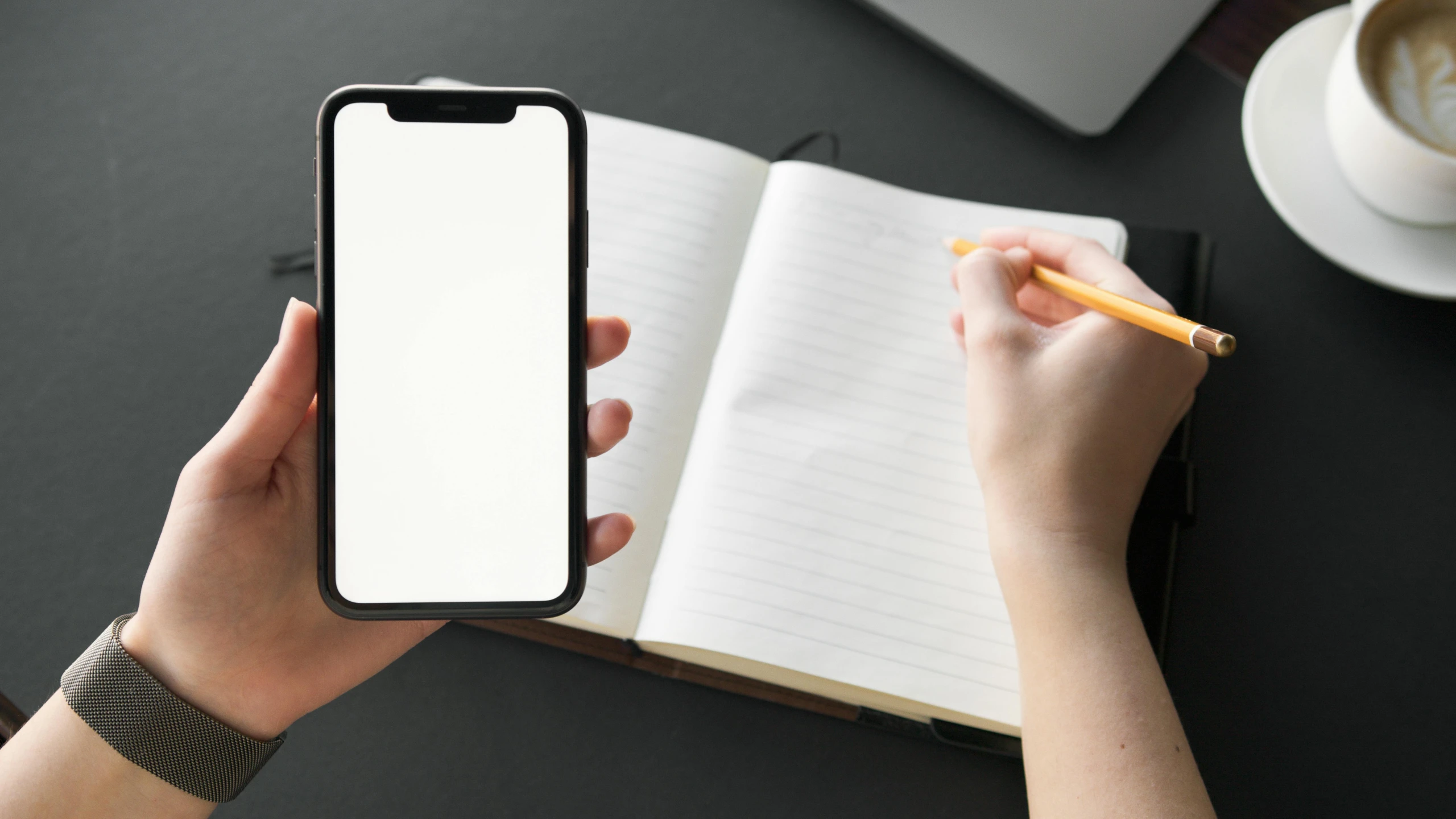 a woman holds up her cell phone and writes on a notepad