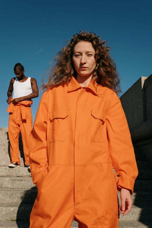 two people stand near the stairs of an orange prison uniform