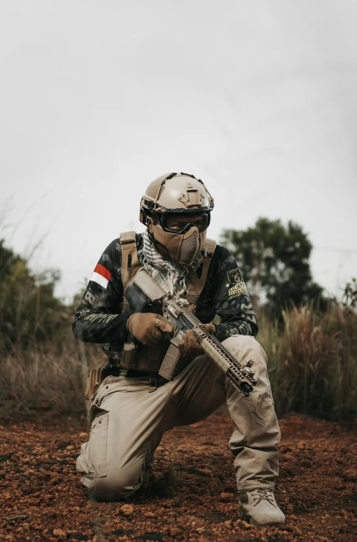 a man kneeling on the ground in a field while wearing an army uniform