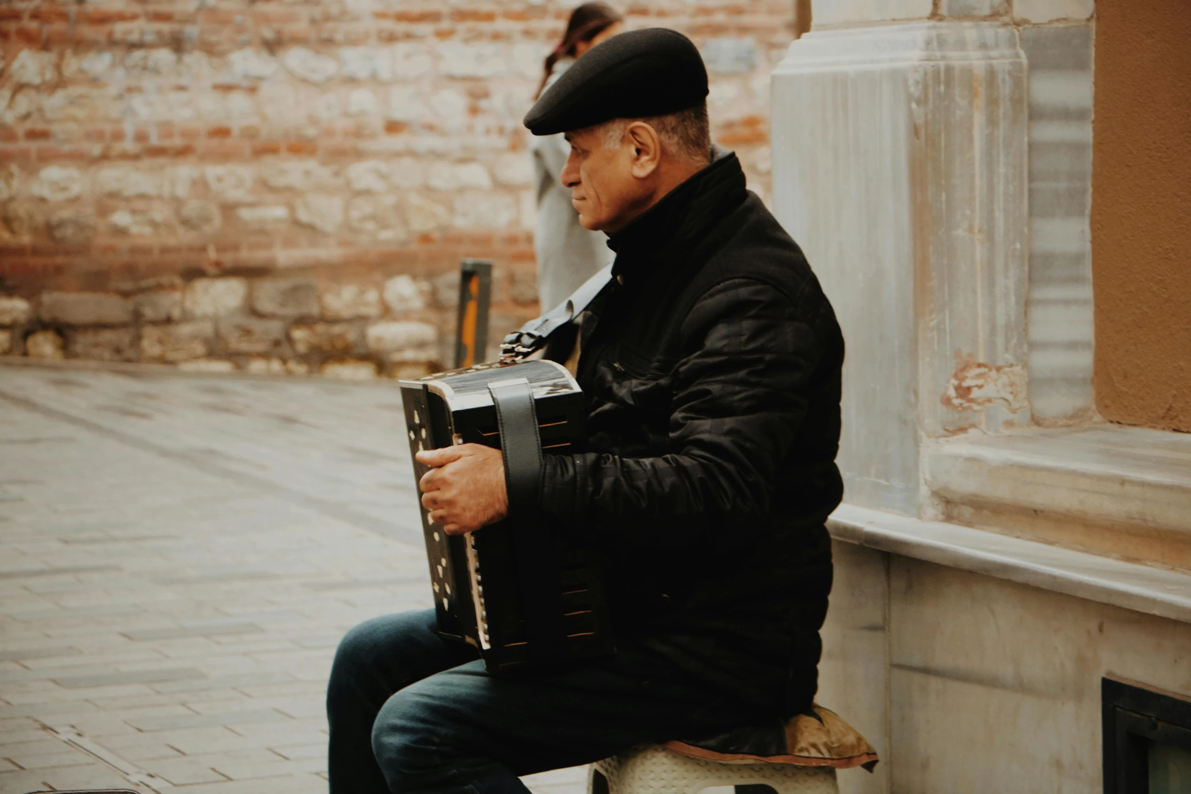 the man sits and plays the accordion by the brick wall