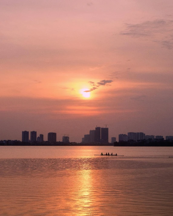 a sunset in the background with buildings on the horizon and boats in the foreground