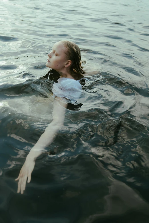 a woman floating in the water wearing a white blouse