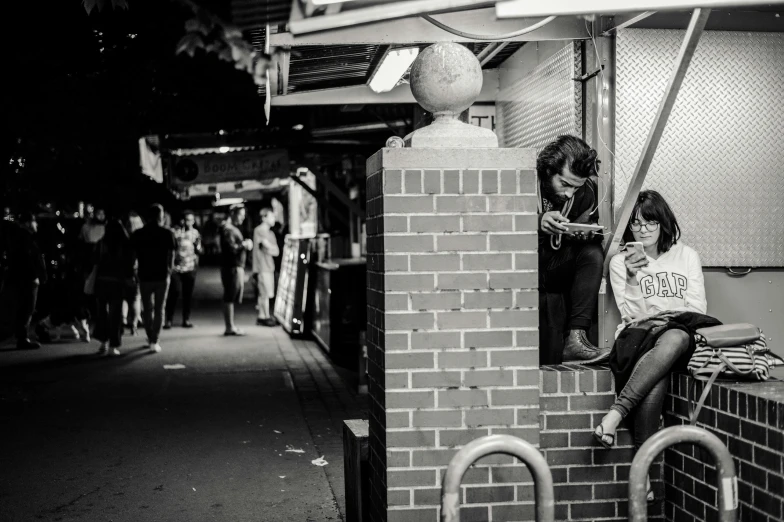 two people are sitting on a brick wall in black and white