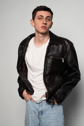 a man wearing a black leather jacket leaning on a grey background