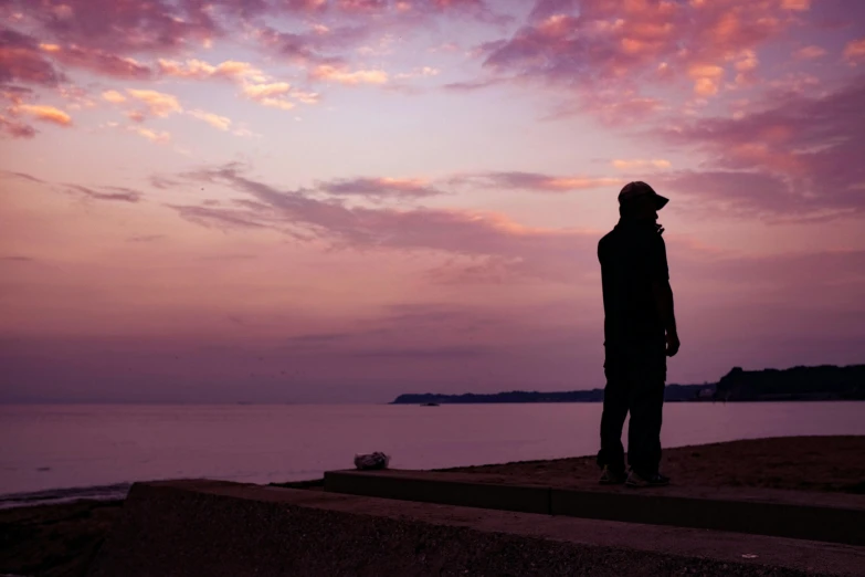 a man standing on a ledge at the ocean with a colorful sunset in the background