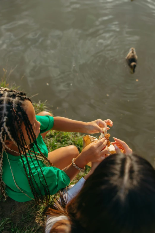 a girl sitting at the edge of a river feeding birds