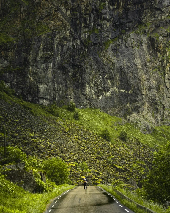 a person riding a motorcycle down a road on a winding green mountain side