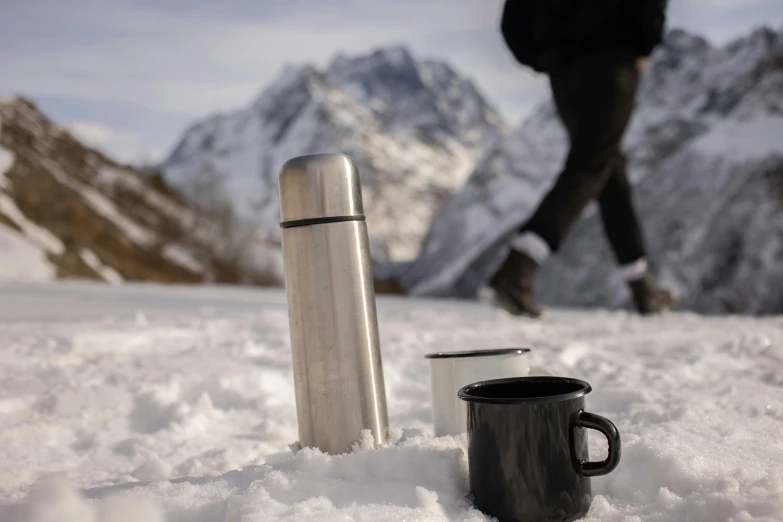 the person is walking in the snow near two mugs